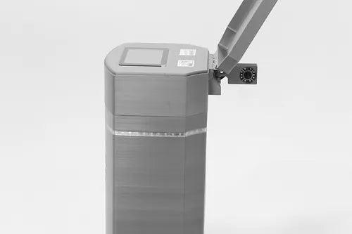 A Poly Lift ICON 4 barrier gate, gray and rectangular with its arm raised and a lift controller attached, features a mounted closed-circuit security camera, set against a plain white background.